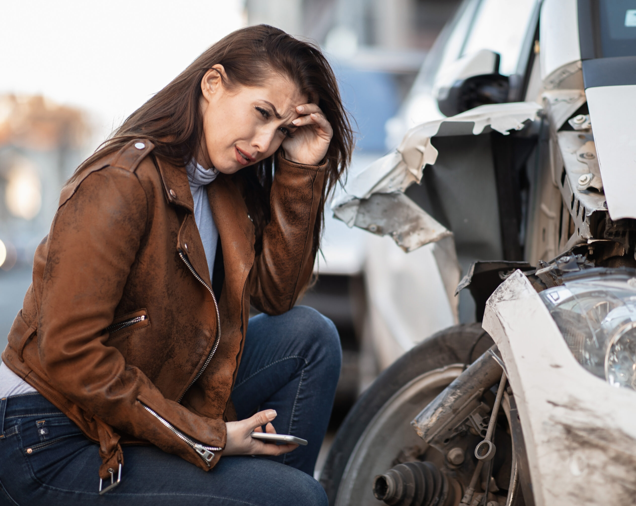 Young woman in despair crying next to her wrecked car.
